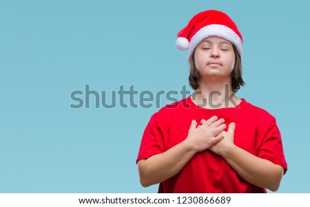 Young adult woman with down syndrome wearing christmas hat over isolated background smiling with hands on chest with closed eyes and grateful gesture on face. Health concept.