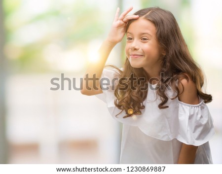 Brunette hispanic girl very happy and smiling looking far away with hand over head. Searching concept.