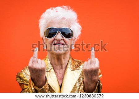 Funny and extravagant senior woman posing on colored background - Youthful old woman in the sixties having fun and partying Royalty-Free Stock Photo #1230880579