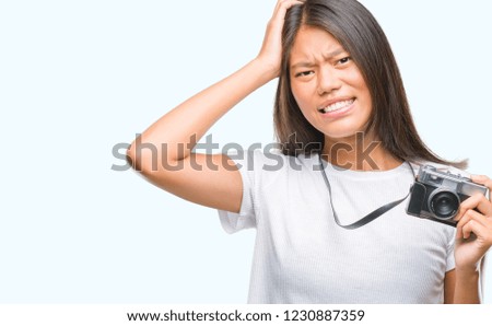 Young asian woman holding vintagera photo camera over isolated background stressed with hand on head, shocked with shame and surprise face, angry and frustrated. Fear and upset for mistake.