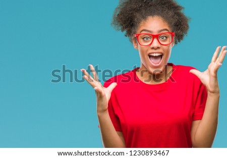 Young afro american woman wearing glasses over isolated background celebrating crazy and amazed for success with arms raised and open eyes screaming excited. Winner concept
