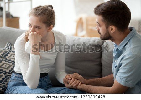 Loving young husband hold crying wife hand showing empathy and support, millennial couple sit on couch at home reconcile after fight, caring man making peace with beloved woman. Relationships concept Royalty-Free Stock Photo #1230899428