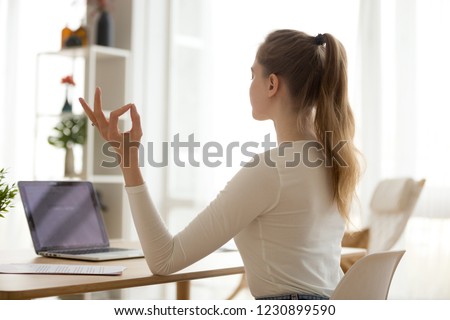 Calm female sit at work desk meditating with hands in mudra position, focused girl practice yoga at office table at home, controlling emotions and relieving stress, woman balance breathing fresh air Royalty-Free Stock Photo #1230899590