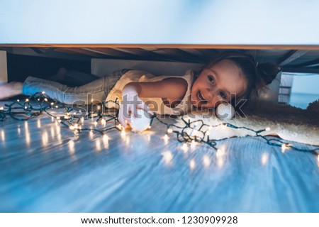 A girl hiding under the bed and playing with a toy and light
