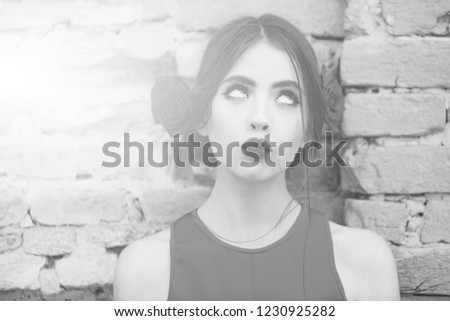 girl. Curious woman or young fashion model with red lips, makeup and fresh roses, flowers in brunette hair, fashionable hairstyle posing outdoors on old brick wall. Beauty and hairdressing salon