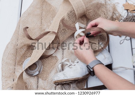 Top view of female hands making Christmas decoration of old vintage ice skates with ribbons, toned