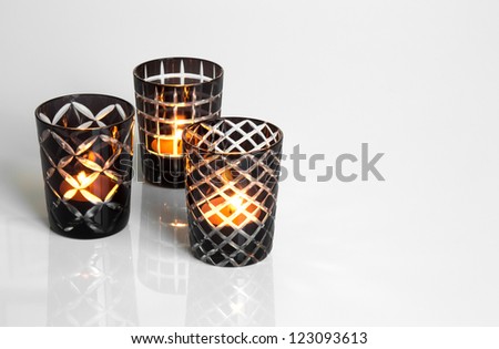 Three tealights in black and white candleholders, on reflective surface.
