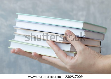 beautiful women's hands holding a stack of colorful books on a concrete background