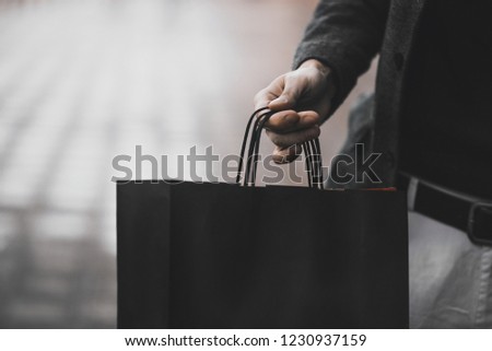 Close up of a young caucasian man holding some different paper shopping bags in the street.
