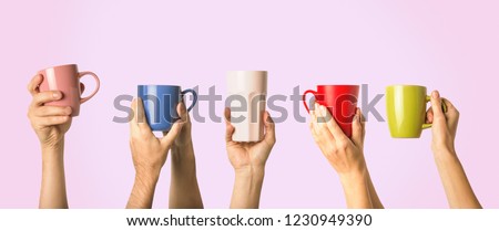 Many different hands holding multi colored cups of coffee on a pink background. Female and male hands. Concept of a friendly team, a coffee break, meeting friends, morning in the team. Banner Royalty-Free Stock Photo #1230949390
