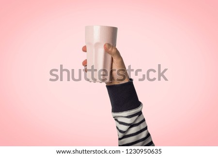 Male hand holding a purple cup with hot coffee or tea on a light pink background. Breakfast concept with hot coffee or tea