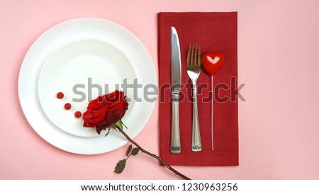 Top view romantic table setting for Valentines day or dinner date celebration wedding. table setting with red rose white plate fork knife on red Viva Magenta tablecloth on pink color background. 