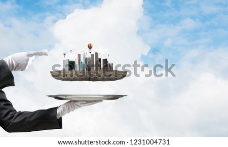 Cropped image of waitress's hand in white glove presenting modern city block on metal tray and pointing on it with blue cloudy skyscape on background. 3D rendering.