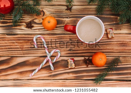 Christmas and New Year pattern. Christmas tree, red cup with coffee, 2 tangerines, candy cane, chocolate bears and Christmas tree toys are lying on the wooden brown background.