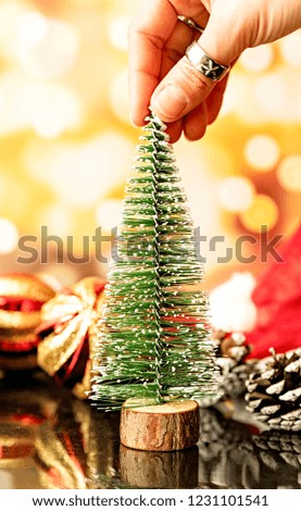 christmas and new year concept. hand holding small christmas tree surrounded with decorations on bright blurry shiny background
