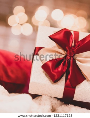 Wrapped gift with red ribbon on fireplace background at home.