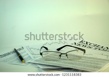 Reading glasses and pen are on the news media.
