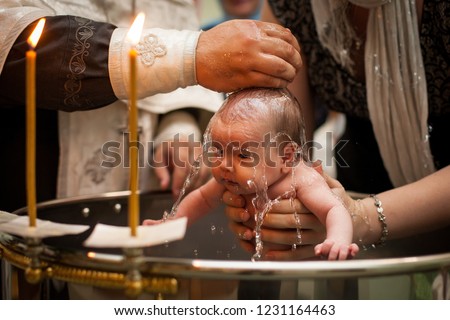 Newborn baby baptism in Holy water. baby holding mother's hands. Infant bathe in water. Baptism in the font. Sacrament of baptism. Child and God. Christening candle Holy water font. The priest baptize Royalty-Free Stock Photo #1231164463