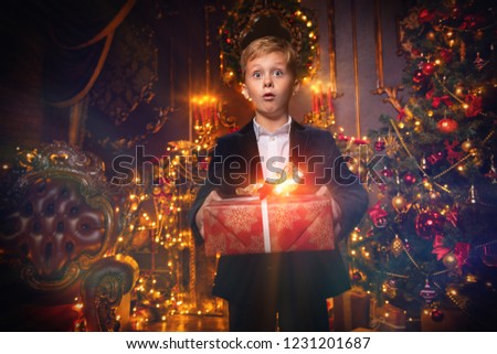 A portrait of a boy with a gift box. Merry Christmas, happy New Year. Luxurious apartment with a christmas tree, lights and decorations. Miracle time and gifts.