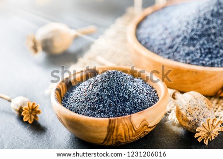 Poppy seeds in small wooden bowl on dark table. Poppies head on board with backlight.