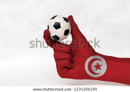 Mini ball of football in Tunisia flag painted hand, hold it with two finger on white background. Concept of sport or the game in handle or minor matter.
