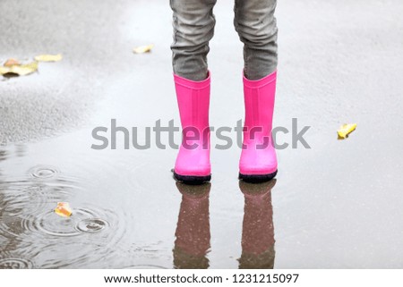 Little girl wearing rubber boots standing in puddle on rainy day, focus of legs. Autumn walk