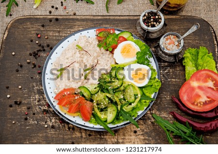 Porridge oatmeal, a salad of tomatoes, cucumbers and peppers and boiled eggs in a light plate on a dark wooden table. Buddha Bowl. Dietary nutrition. Healthy and tasty breakfast. Fitness menu.