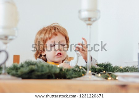 Baby in pajamas holding Christmas toy deer, festive table