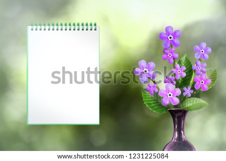 Beautiful live forage bouquet bouquet in ceramic vase on sunny day with notebook with blank place for your content on natural leaves and sky blurred bokeh background.
