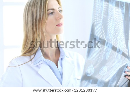 Doctor woman osteopathist examining x-ray picture while standing near window in clinic or hospital. Medicine and healthcare concept
