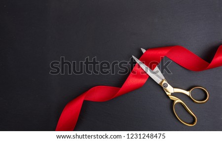 Grand opening. Top view of gold scissors cutting red silk ribbon against black background, copy space Royalty-Free Stock Photo #1231248475