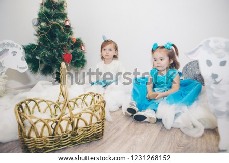 a little girls in a blue dress celebrates the new year: a child among the snow of cotton wool, painted sheep, Christmas tree and stars