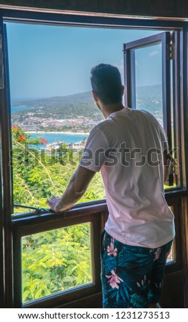 Man admiring view of beach coast and trees, from the window above. Shot in Montego Bay, Negril Beach, Jamaica, Caribbean
