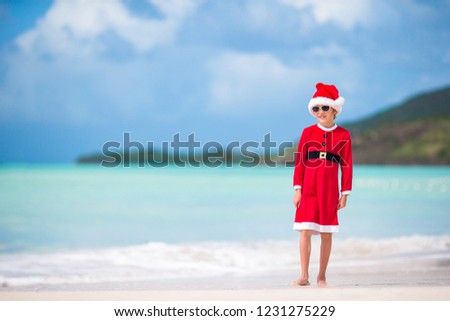 Happy little girl in Santa hat and costume on tropical beach