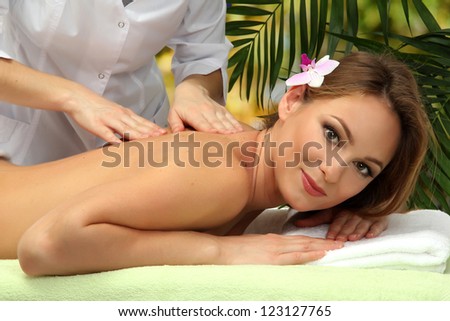 beautiful woman in spa salon  getting massage, on palm leaves background