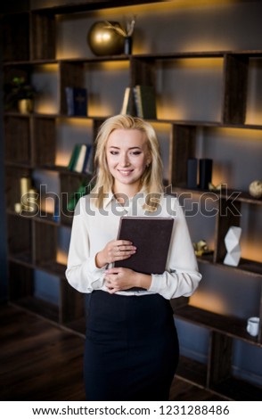 beautiful young business lady is Standing in a black skirt and white blouse in her office with documents. Business concept