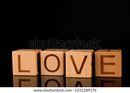 Wooden cube with word "LOVE" on black reflective table