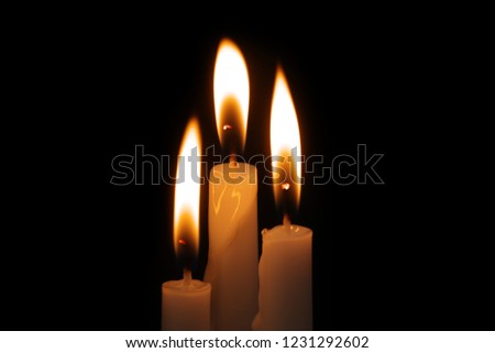 Three burning candles in darkness close up. Religion and memorial concept and symbol.
