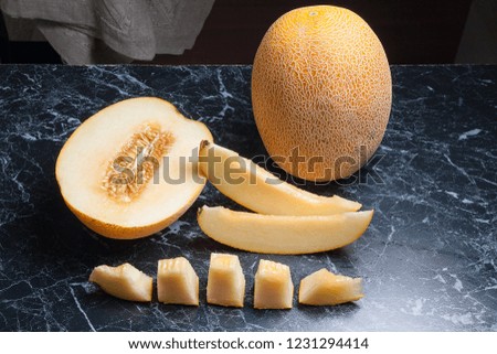Ripe whole and half honeydew melon fruit at summer time. Sliced ripe juicy melon fruit on dark marble background.
