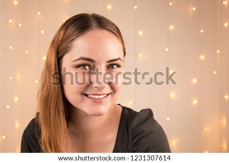 Headshot of beautiful young woman smiling with christmas lights garland on background Toned.