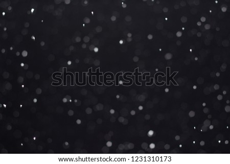 Abstract bokeh background. Dark Christmas background with white round spots from falling snow.