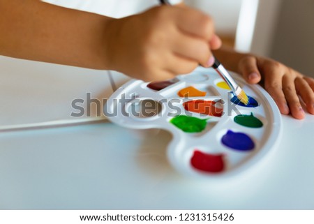 Closeup of paintbrush in kid`s hands mixing paints on palette