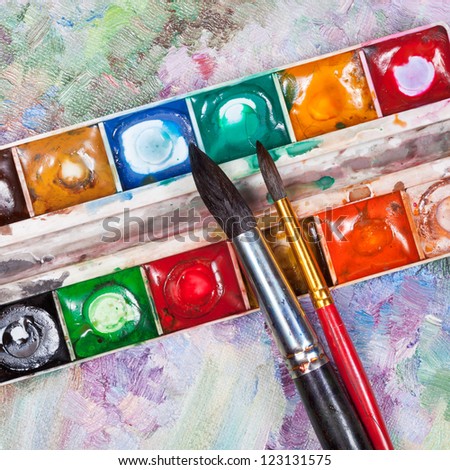 old used watercolor set and two brushes on oil picture background