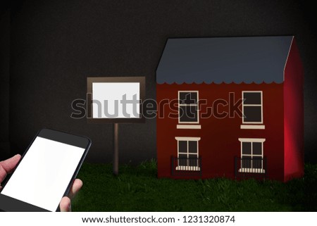 Hand holding white smartphone screen and red house with blank wood sign in the garden, copy space idea