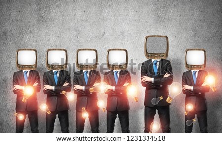 Businessmen in suits with old TV instead of their heads keeping arms crossed while standing in a row among flying lightbulbs in empty room with gray wall on background.