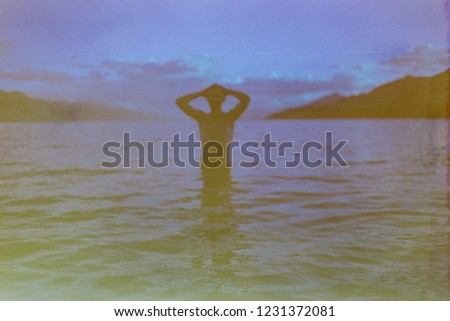 Film photography, a blurry, moody postcard of a person in the lake between mountain, with a nostalgic vintage feeling