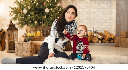 Mother with her son sitting on the carpet and playing against the background of the Christmas tree and gift boxes.
