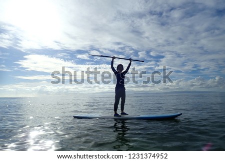 An asian woman holding up the paddle on the stand up paddle board in the calm sea in Oslob, Cebu, Philippines.