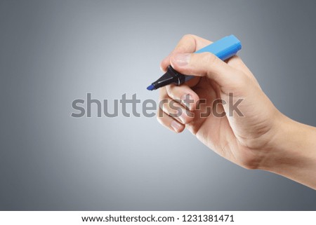 Hand holding a blue marker on grey background