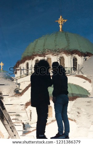 Blurry reflection of Saint Sava orthodox temple and two men standing in front, on wet city pavement in Belgrade, Serbia